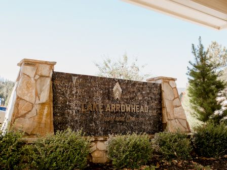 A stone entrance sign reads &ldquo;LAKE ARROWHEAD,&rdquo; with a waterfall feature and landscaped shrubs under a bright sky.