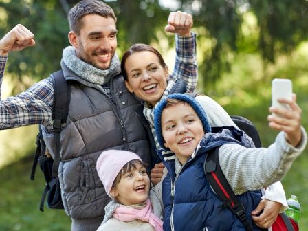 Happy family takes a picnic selfie outdoors, with parents and kids smiling and making playful fist poses.