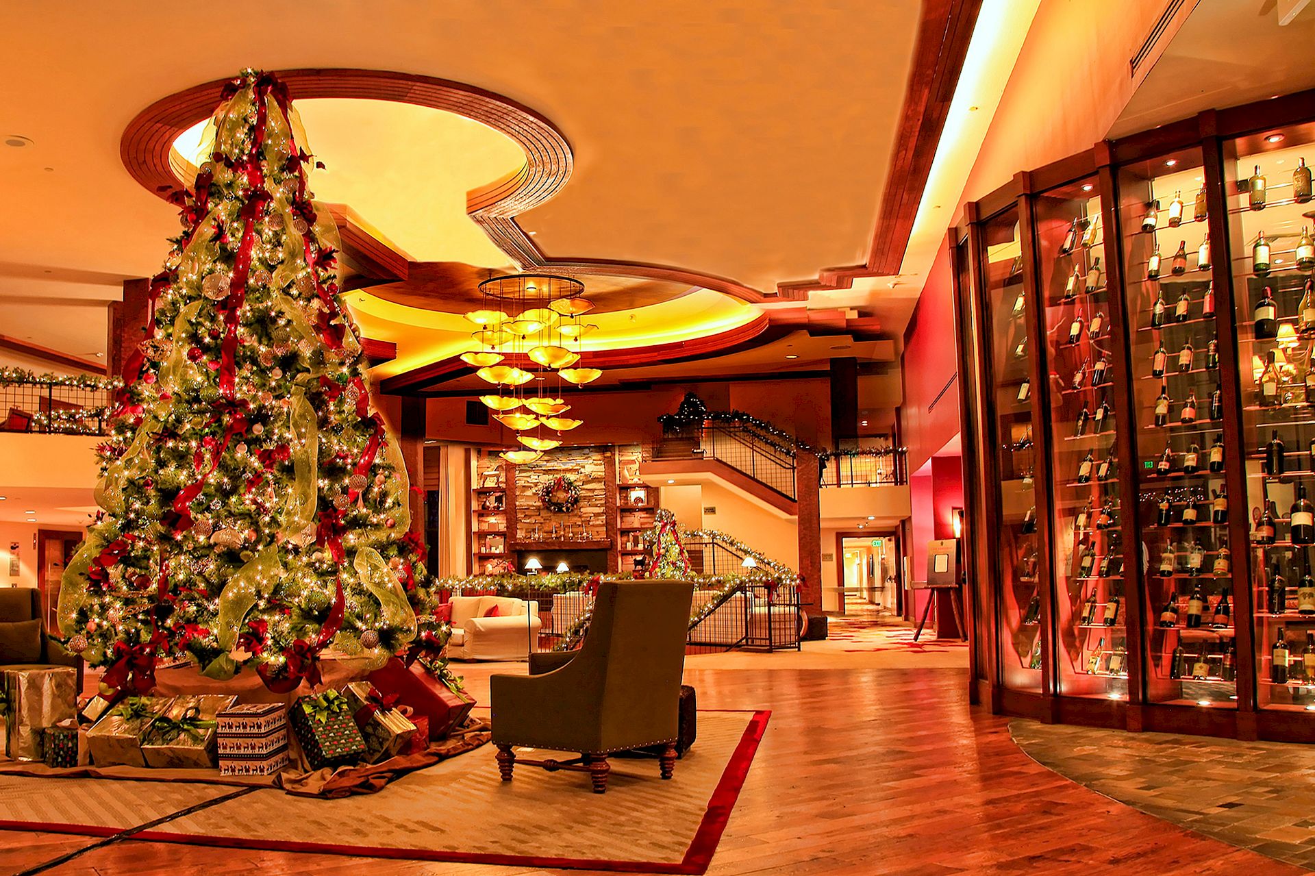 A large decorated Christmas tree stands in a hotel lobby beside a sparkling display of wine bottles and warm holiday lighting.
