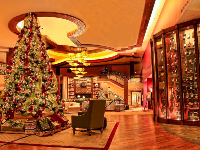 A huge decorated Christmas tree lights up a festive hotel lobby beside a glass display of wine bottles and warm lights.
