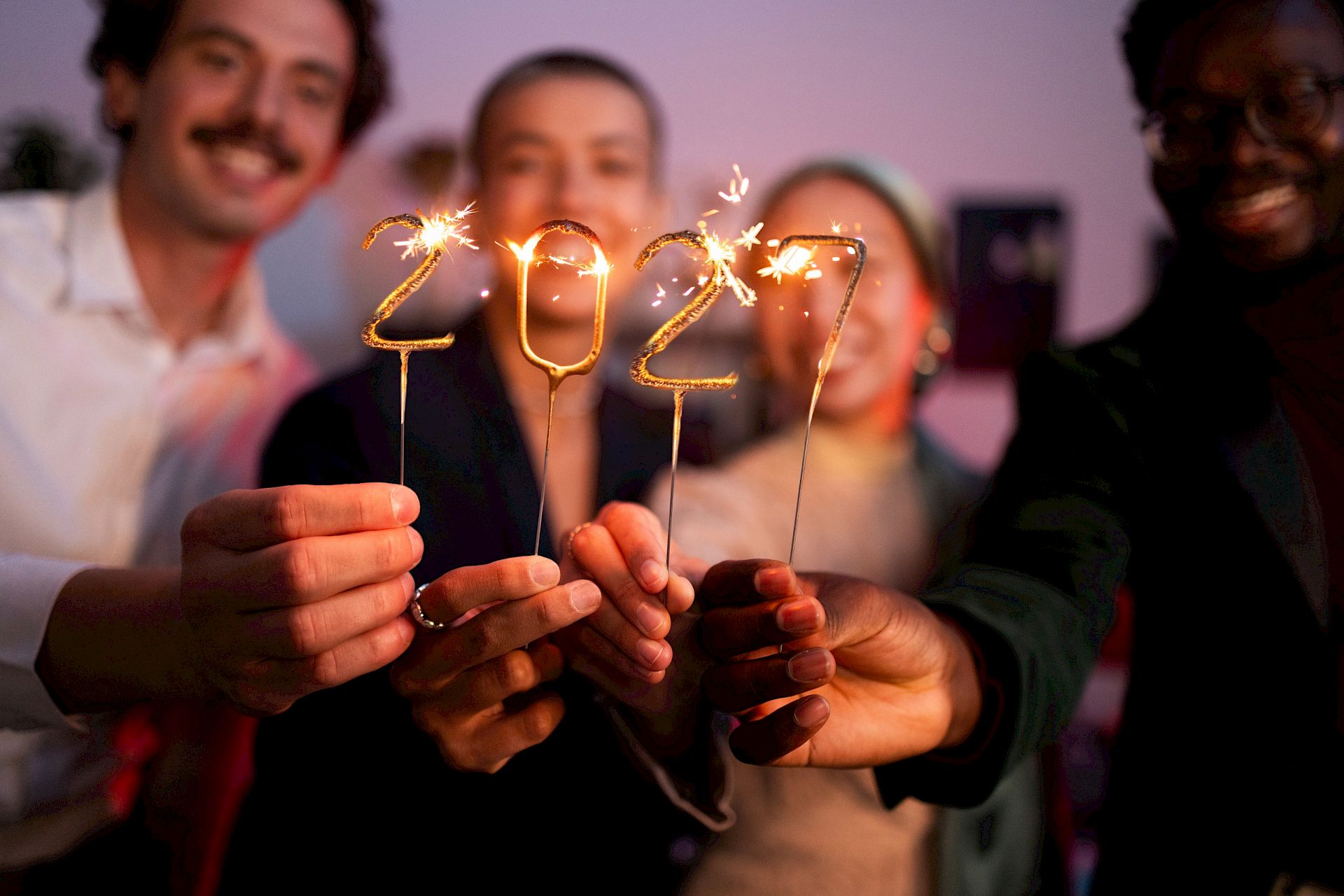Friends celebrate with sparkling candles spelling &ldquo;2019,&rdquo; smiling together in a party setting.