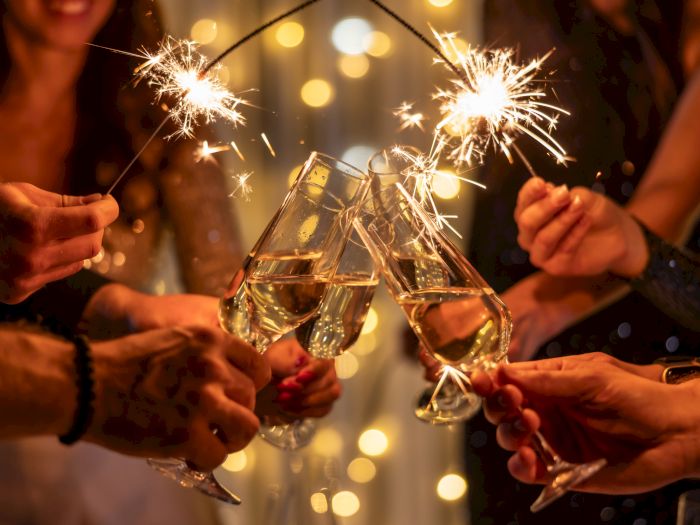 Friends clink champagne flutes with sparklers in a warm, celebratory toast, bright sparks lighting up the night.