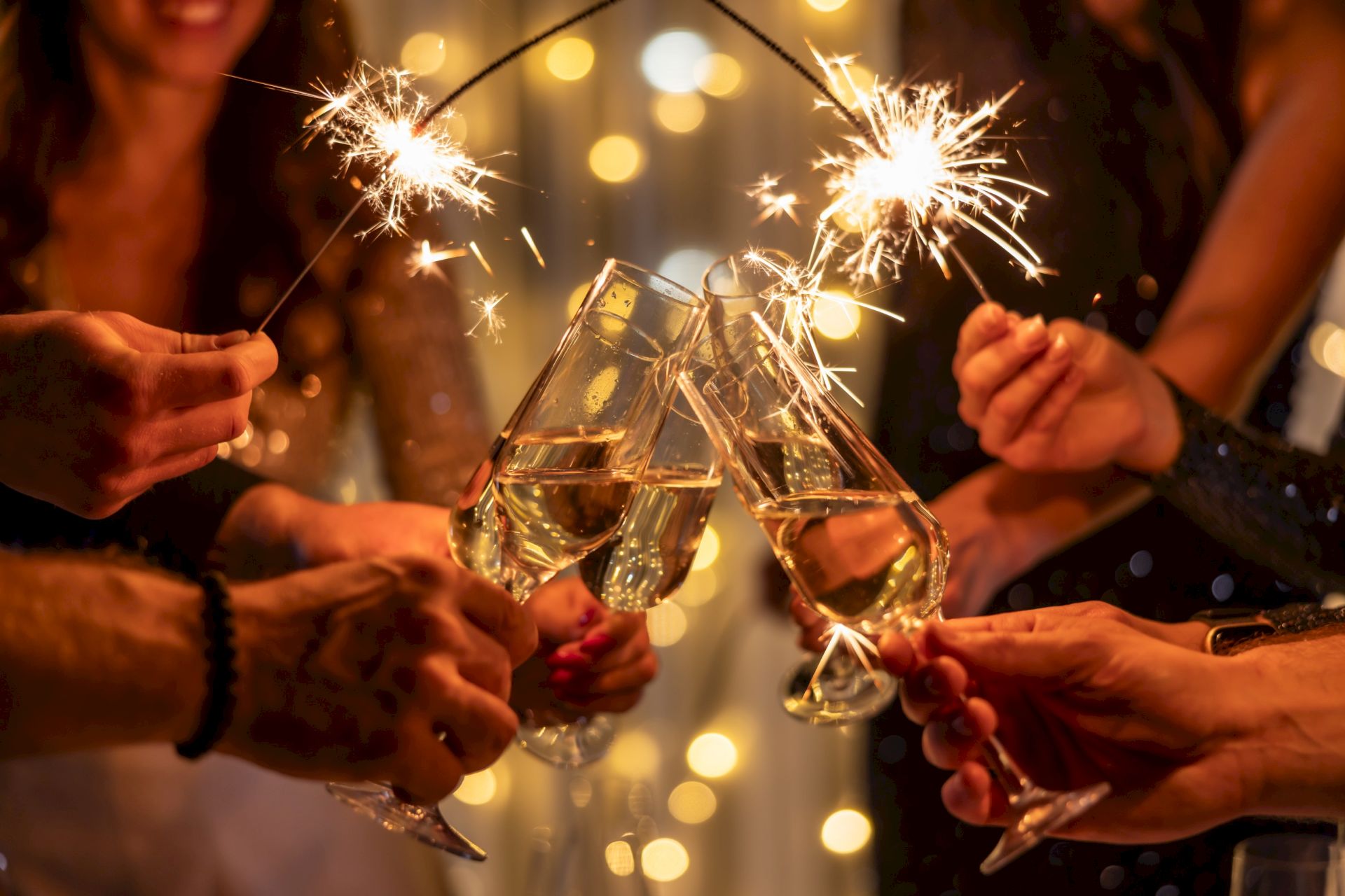 Friends clink champagne flutes with sparklers, celebrating together as bright sparks light up the party.