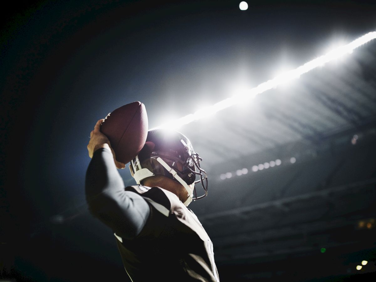 A football player is preparing to throw a pass under bright stadium lights during a nighttime game.