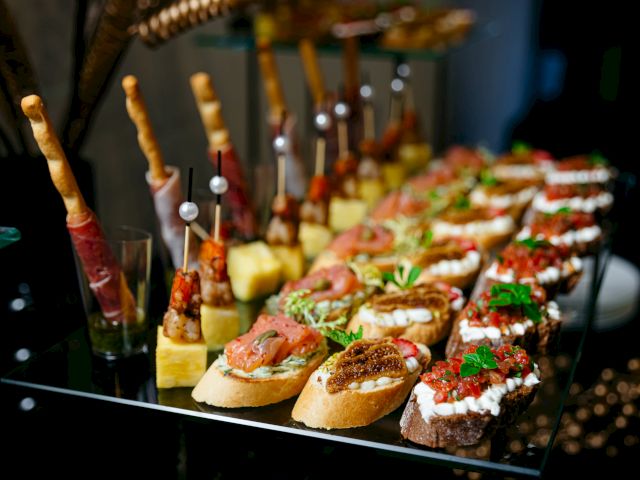 A selection of assorted appetizers on a glass plate, including bruschetta, skewers, and breadsticks wrapped in prosciutto.