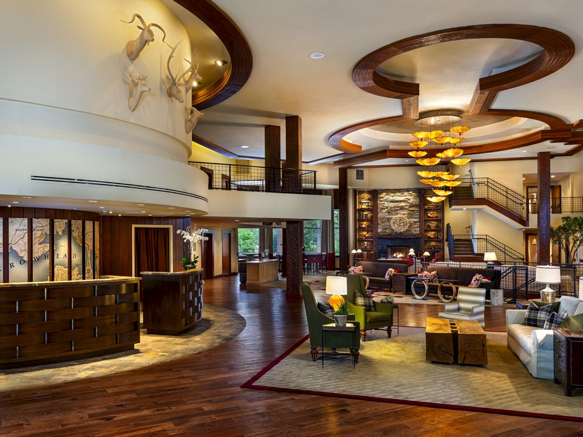 A spacious, elegant hotel lobby with wooden floors, stylish decor, seating area, and a reception desk, featuring a fireplace and sculptures.
