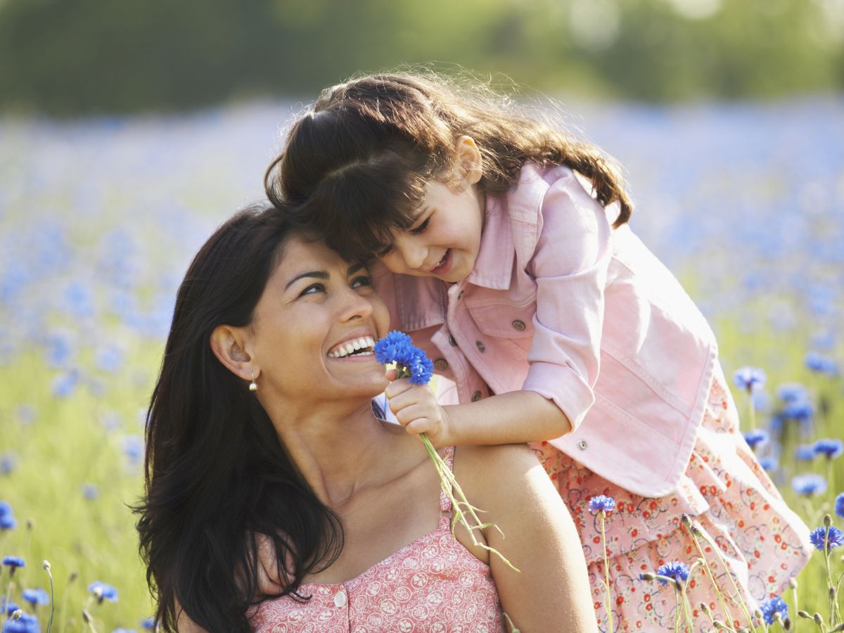 A woman and child smiling in a field of blue flowers, with the child holding a flower.