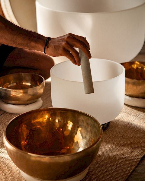 A hand is playing crystal and brass singing bowls, often used for meditation and sound healing practices.