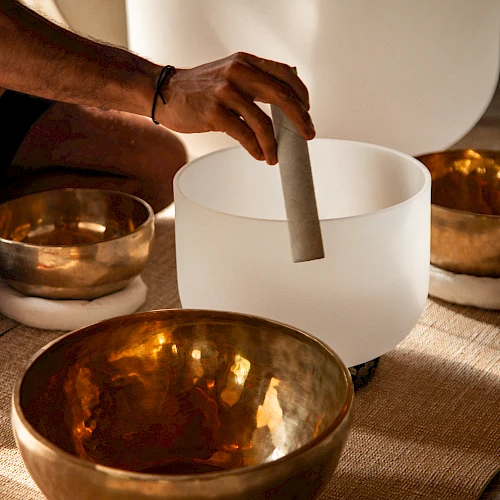 A hand is playing crystal and brass singing bowls, often used for meditation and sound healing practices.