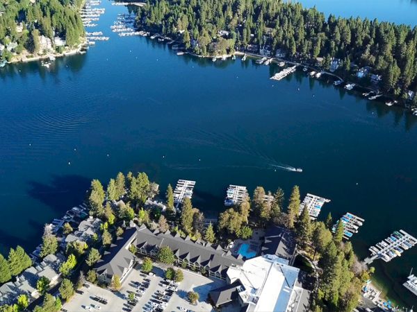 Aerial view of a serene lake surrounded by dense trees, with numerous boats docked along the shoreline in a picturesque setting.