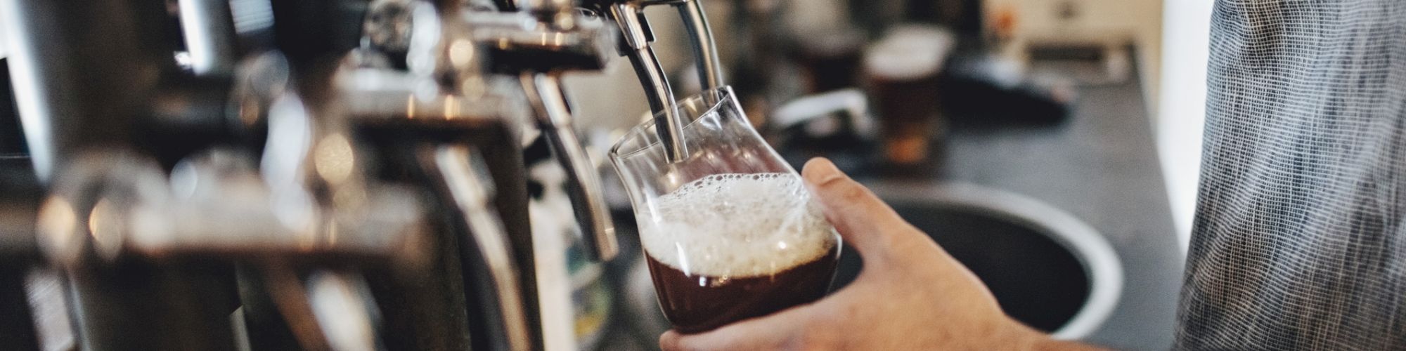A person is pouring a draft beer into a glass from a tap in a bar or brewery setting.