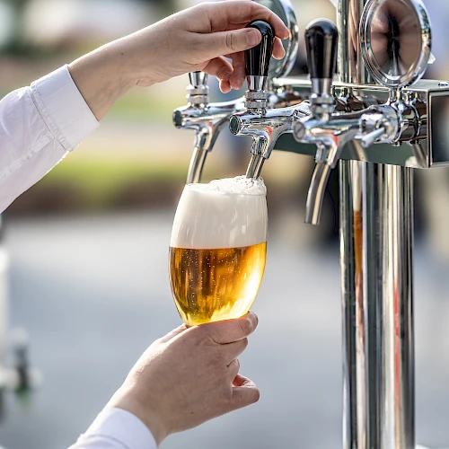 A person is pouring beer from a tap into a glass, creating a frothy head.