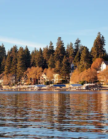 Autumn lakeside scene with golden trees, cottages and docks along the water under a bright blue sky.