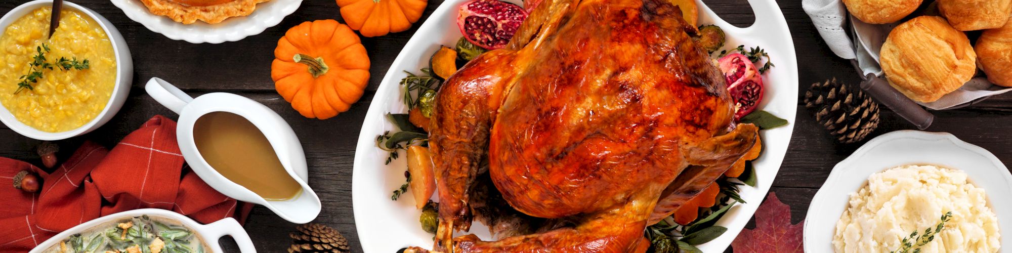 Thanksgiving feast with a roasted turkey, pumpkin pie, mashed potatoes, stuffing, rolls, and other side dishes on a table.