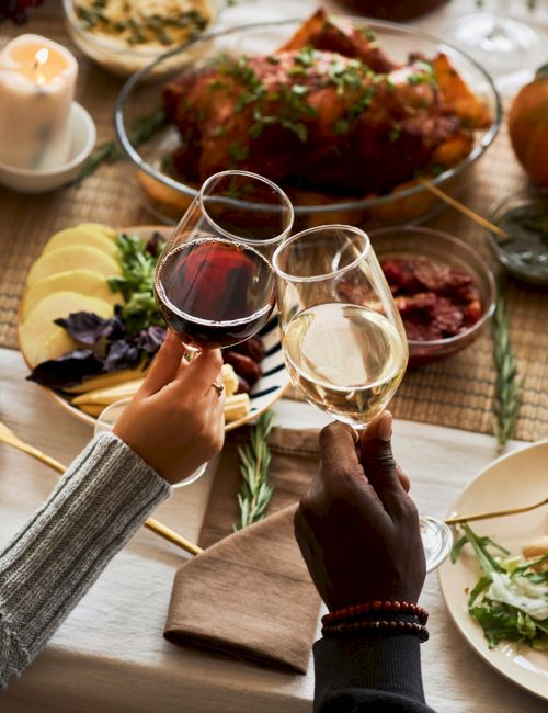 A festive table setting with various dishes, candles, and two people toasting with glasses of wine, creating a warm, cozy atmosphere.