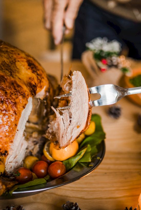 A person carves a roasted turkey on a table set with salads and a candle, creating a festive dining atmosphere.