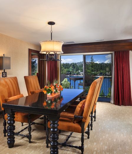 A hotel-style dining room with a large table, leather chairs, chandelier lighting, stone fireplace, and large glass doors.