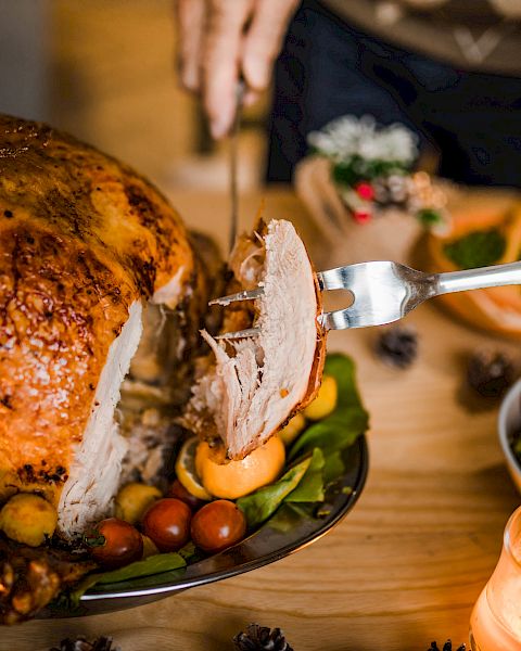 A person carves a roasted turkey on a table set with various dishes, including salads and sides, under warm candlelight.