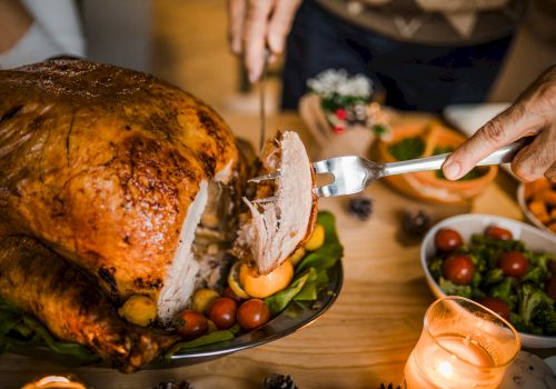 A person carves a roasted turkey on a table set with various dishes, including salads and sides, under warm candlelight.