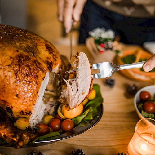 A person carves a roasted turkey on a table set with various dishes, including salads and sides, under warm candlelight.