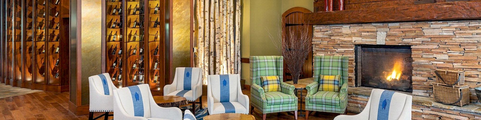 A cozy lounge with white and blue chairs, wooden coffee tables, a stone fireplace, brick walls, a TV, and a wine rack area.