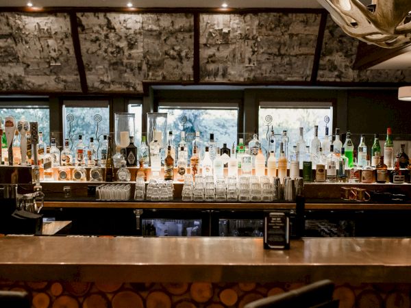 The image shows a bar with a variety of liquor bottles lined up on shelves and a countertop in front.