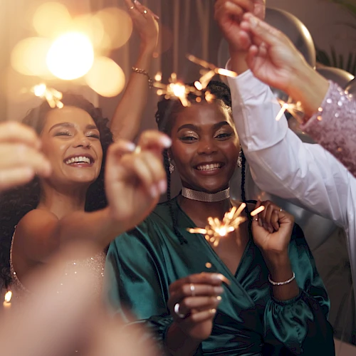 A group of friends at a celebration, holding sparklers and smiling as they toast and enjoy a festive night together.