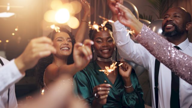 A group of friends at a celebration, holding sparklers and smiling as they toast and enjoy a festive night together.