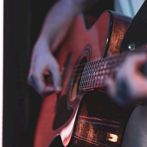 A person plays an acoustic guitar, strumming near a neon-lit edge, focus on strings and frets with a moody, intimate vibe.