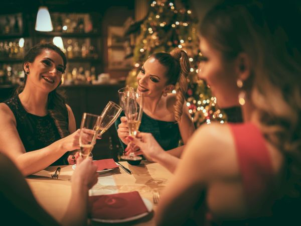 Three friends toast with champagne glasses at a warmly lit dinner, smiling and enjoying a festive night.