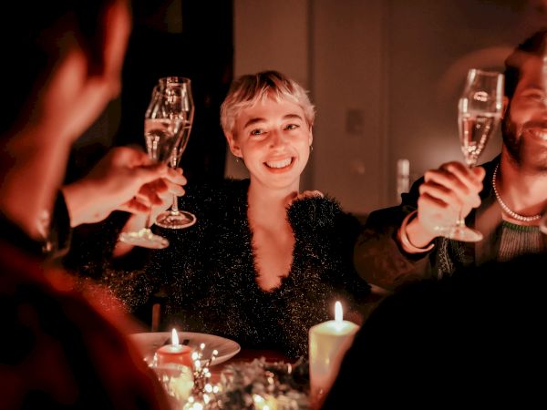 A group of people at a dinner party toasting with champagne flutes, warm candles, smiling faces, and a cozy, festive vibe.