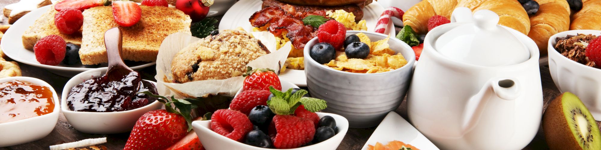 A festive breakfast spread: pastries, berries, candy canes, yogurt bowls, pancakes, croissants, salmon, nuts, honey, coffee, and juice, abundant treats.