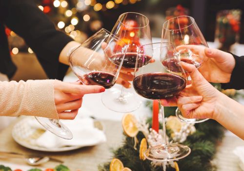 Friends toast with wine glasses around a festive table, holiday lights and a centerpiece bring warm, celebratory vibes to the scene.