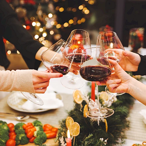 Friends toast with wine glasses around a festive table, holiday lights and a centerpiece bring warm, celebratory vibes to the scene.