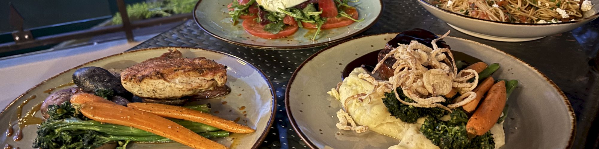A table of four plates with assorted dishes: grilled salmon/vegetables, a salad with greens and sliced proteins, a pasta dish, and a creamy roasted veg plate.
