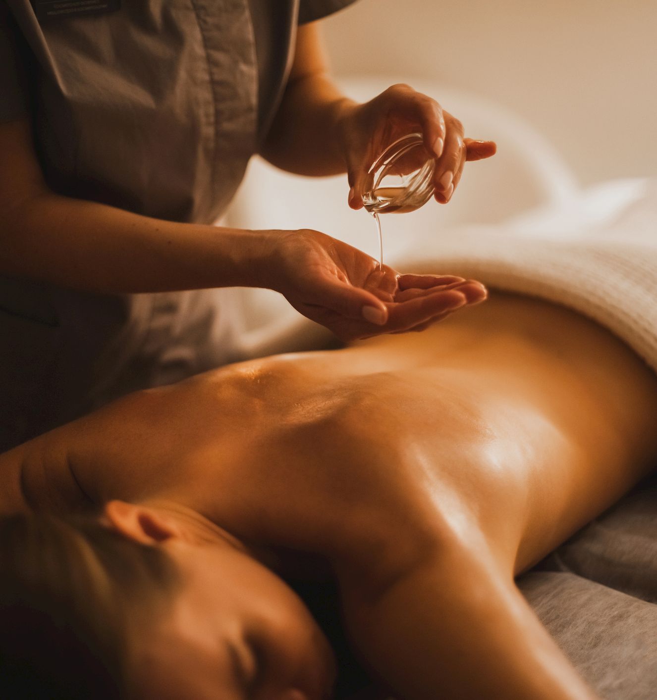 A person receives a massage or spa treatment; a therapist applies oil to the back of a lying client, with soft lighting and towels.