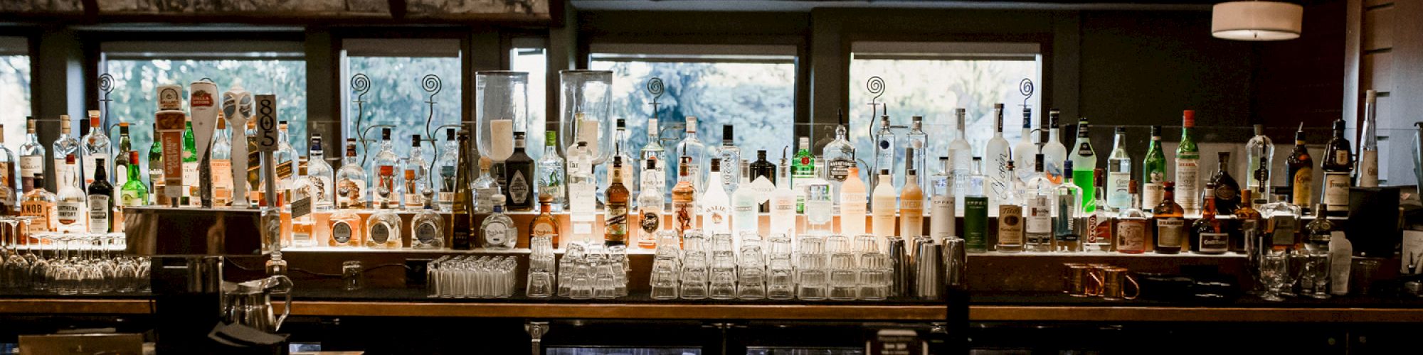 A bar with a long display of assorted bottles behind the counter, dim lighting, and a rustic, cozy vibe.