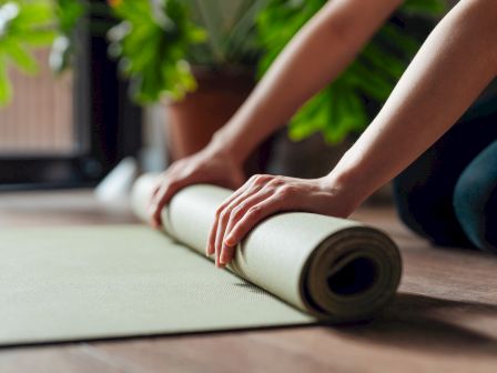 A person is rolling out a yoga mat on the floor, hands firmly pressing the mat as it unfurls.
