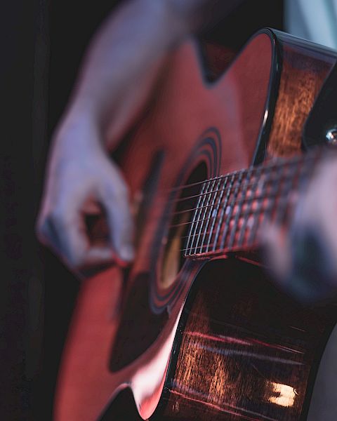 A close-up of a person playing an acoustic guitar, focusing on the strings and fretboard, with a soft pink light in the background, artistry in motion.