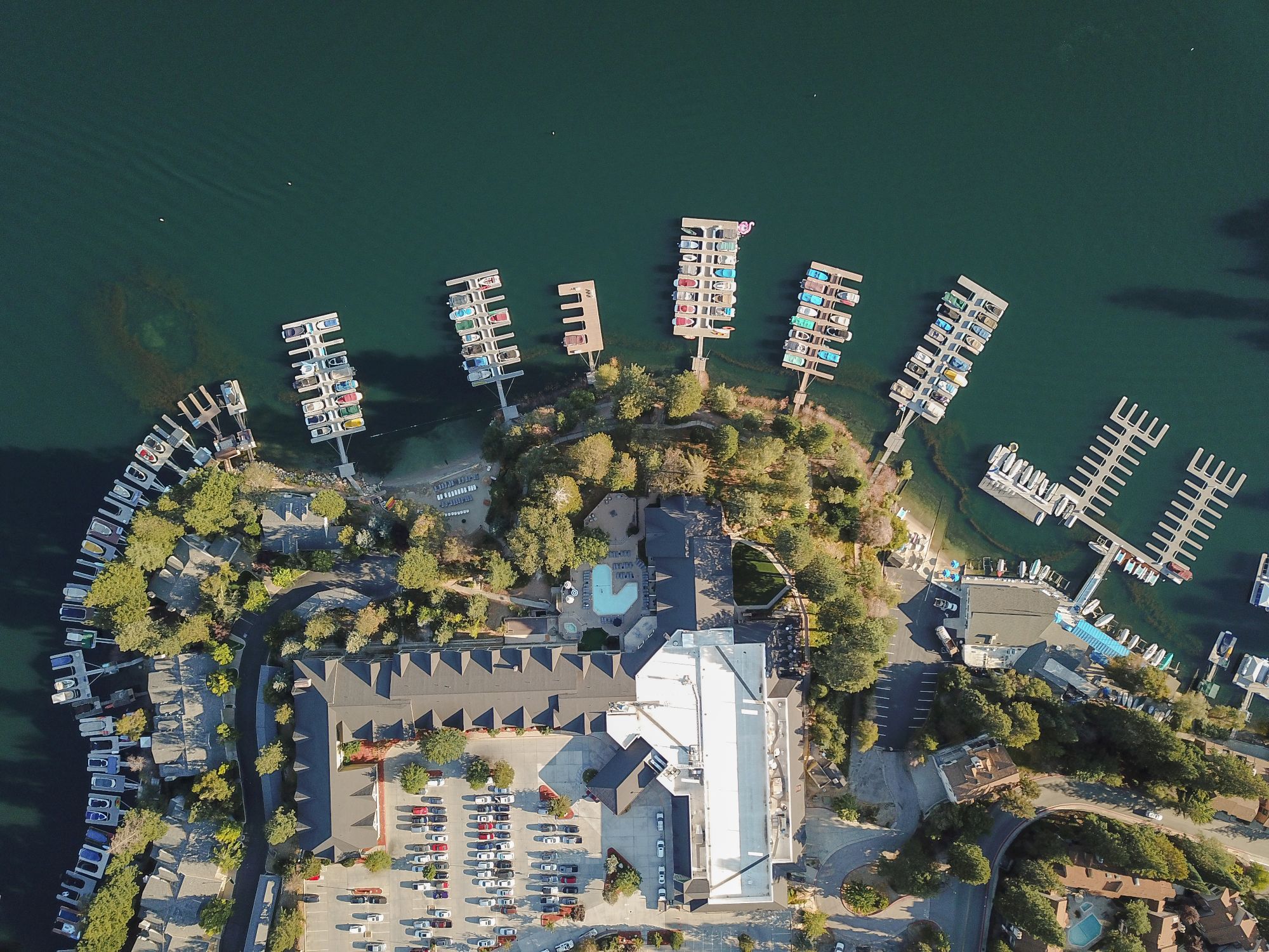 Aerial view of a marina with many docked boats, piers, and a riverside parking area.