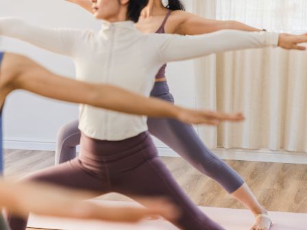 People practicing yoga in a studio, doing side stretches with outstretched arms, wearing athletic wear on a wooden floor.