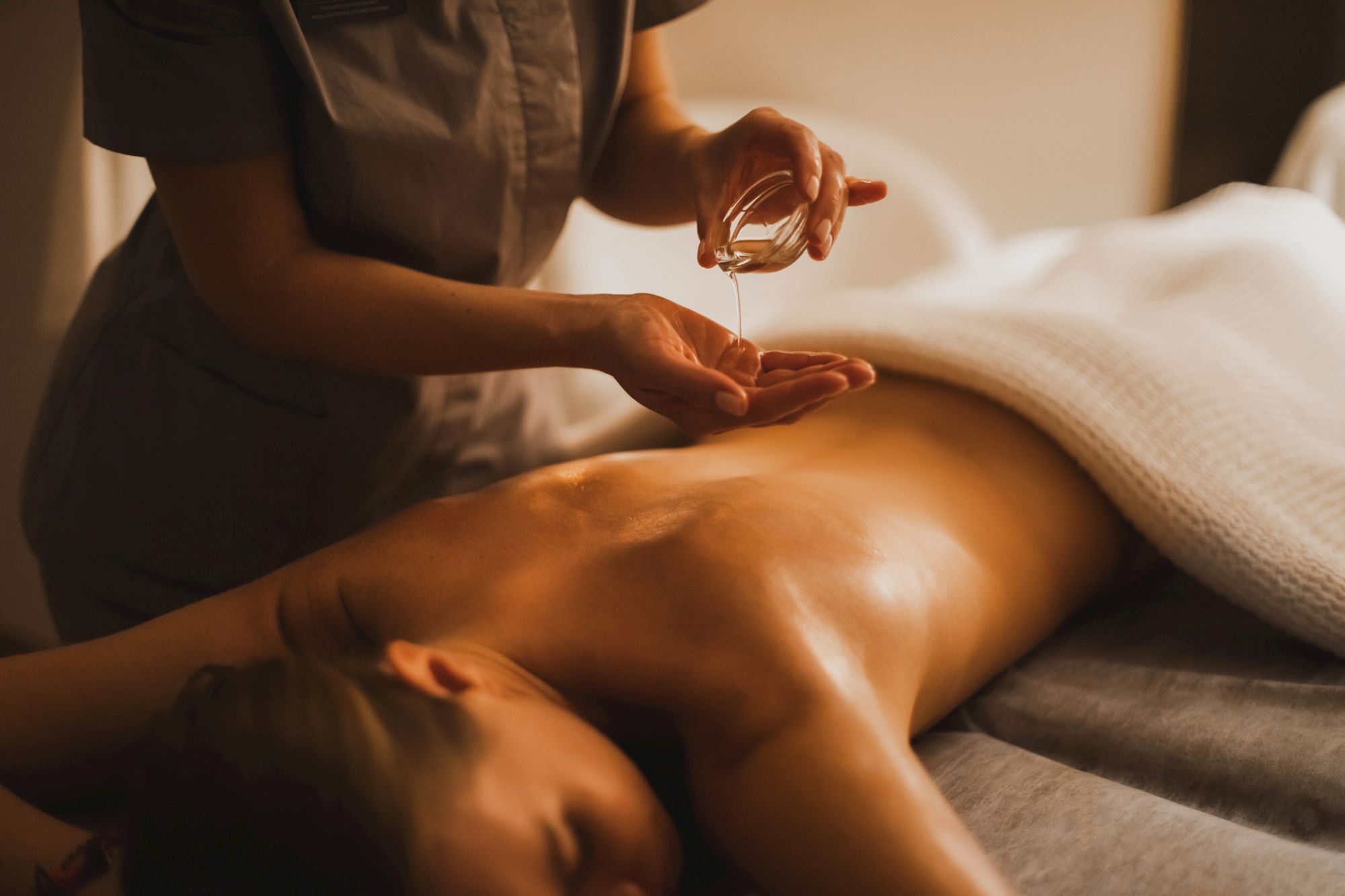 A person receiving a massage or spa treatment; a therapist applies oil to a bare back on a massage table, creating a calm, relaxing setting.