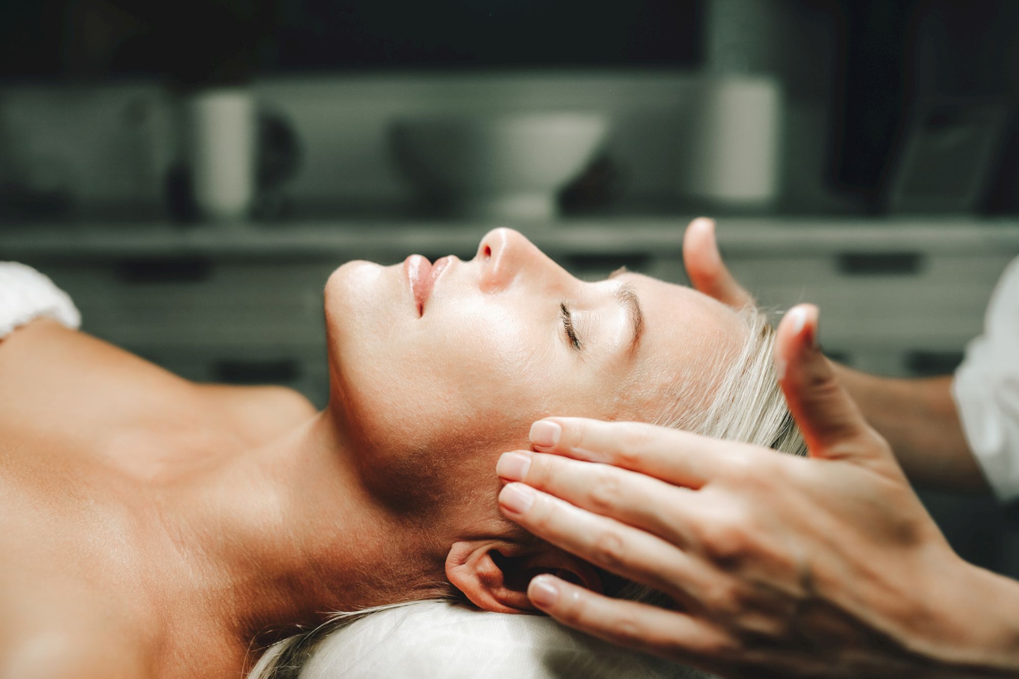 A man receiving a relaxing head/face massage, with hands gently pressing along his forehead and temples.