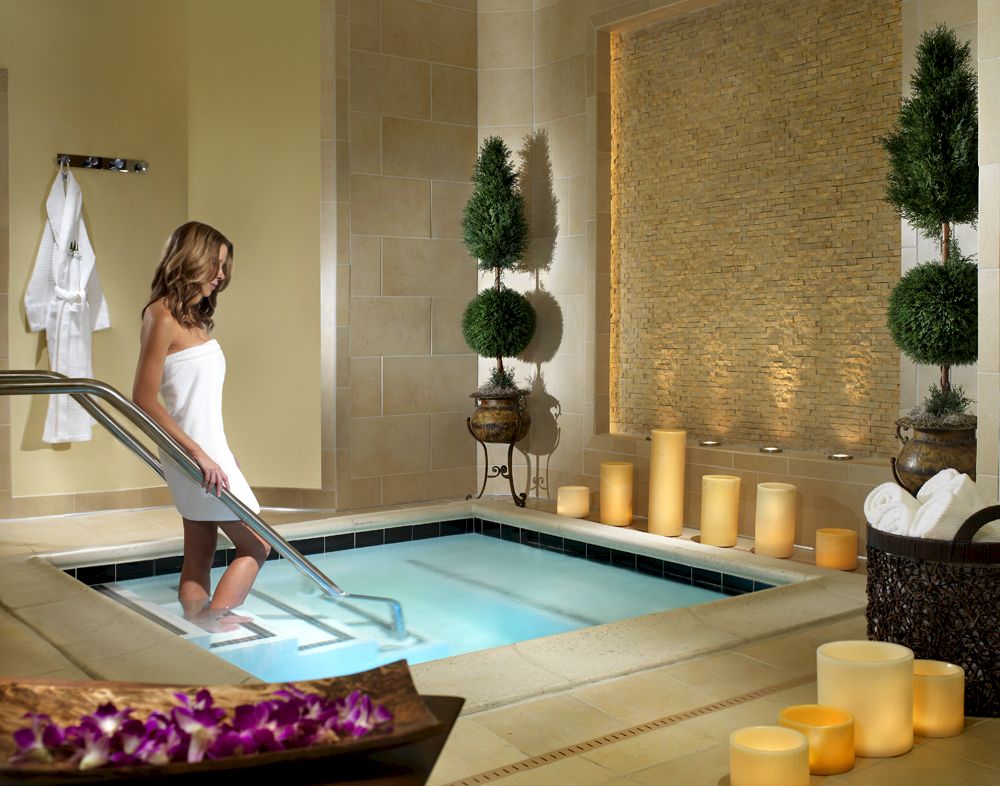 A woman relaxes at a hotel spa pool while candles glow around the tiled room, creating a calm, luxurious atmosphere.