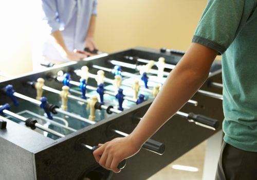 A person playing on a foosball (table soccer) table, moving the rods with their hands to control the players.
