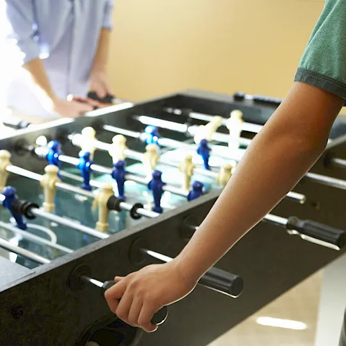 A person playing on a foosball (table soccer) table, moving the rods with their hands to control the players.