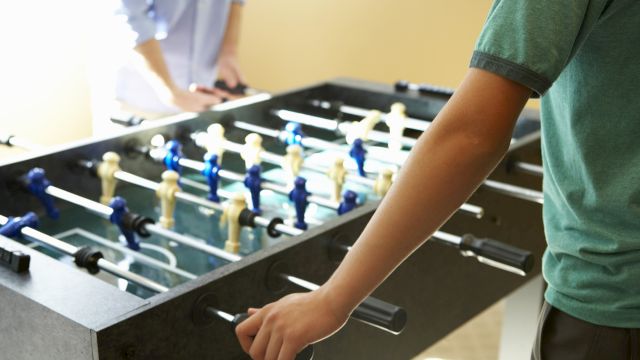 A person playing on a foosball (table soccer) table, moving the rods with their hands to control the players.