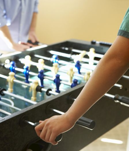 A person plays foosball, gripping the handles as colorful players line up on the table.