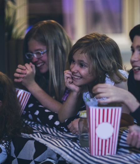 A group of kids laughing during a movie night, sharing popcorn and drinks together.